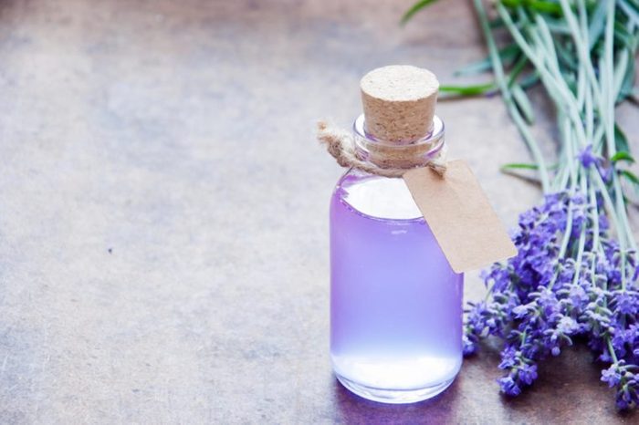 lavender oil in a clear bottle and lavender flowers on a table