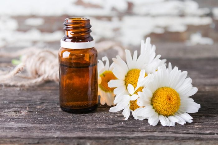 chamomile oil bottle next to sunflowers on wooden table