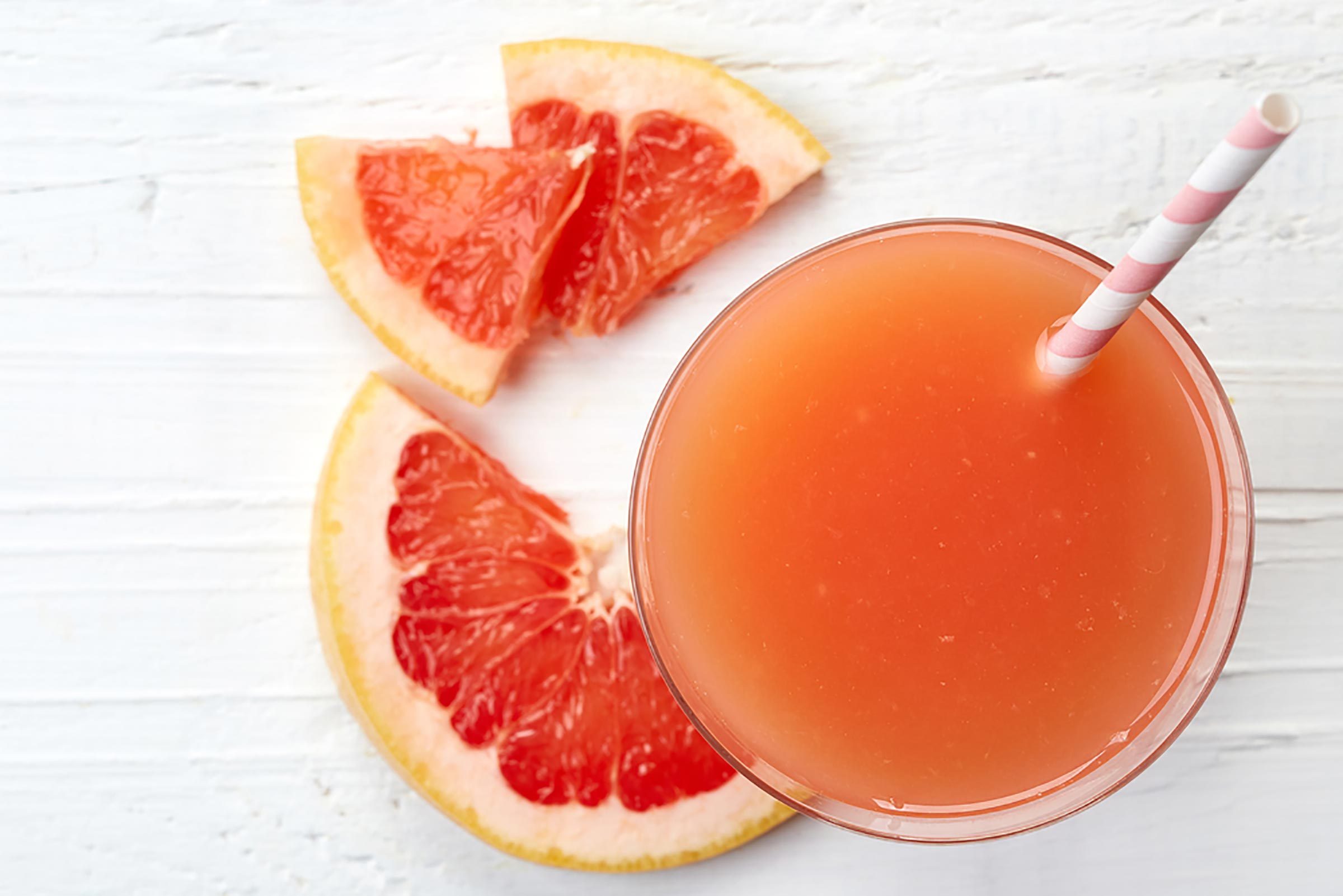 стакан грейпфрутового сока с розово-белой полосатой соломинкой