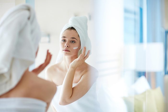 woman with towel wrapped around her head applying face cream