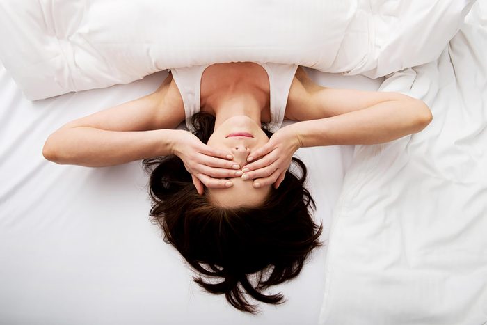 Woman with hands over eyes in bed