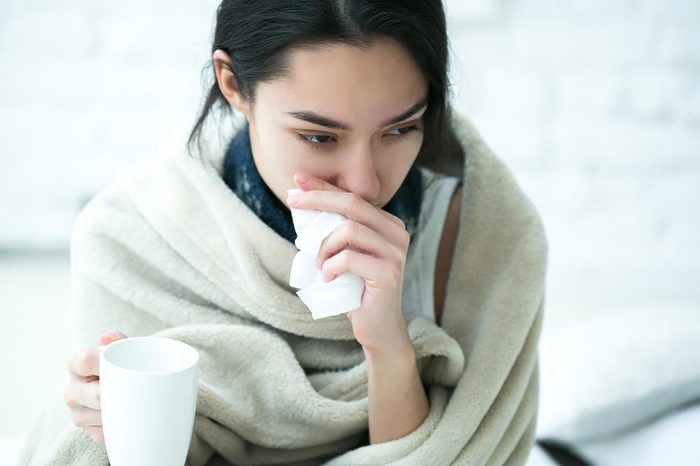 woman bundled up with tea holding a tissue