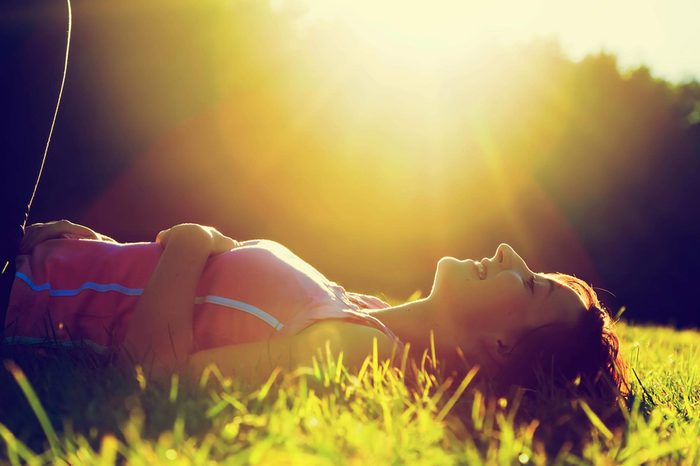 A woman lying in the grass outdoors in the sunlight.