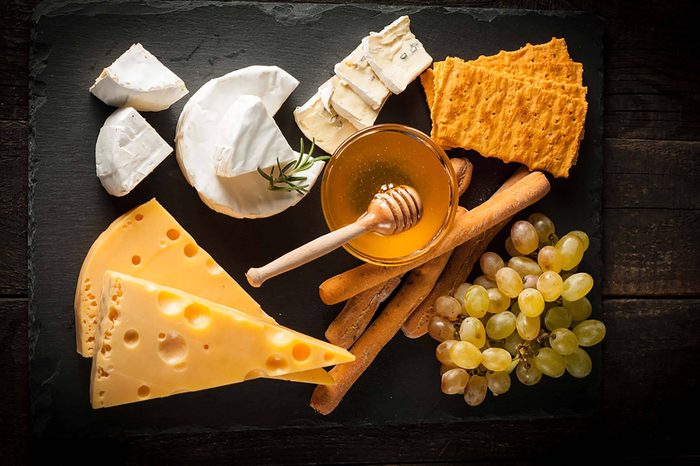 varieties of cheese with crackers, honey, and grapes