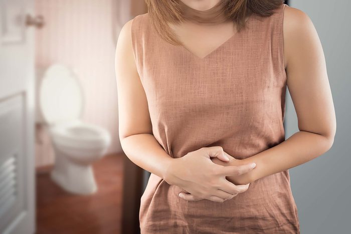 Woman clutching her stomach with bathroom in background