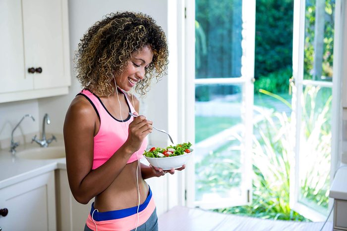 Woman in exercise gear eating a salad in her kitchen.