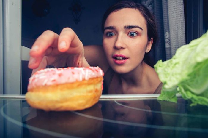 Woman reaching for donut instead of lettuce in refrigerator 