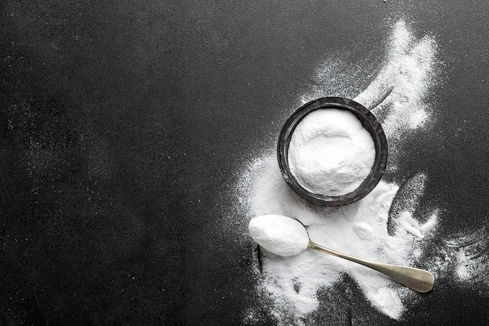 Baking soda powder in a bowl, on a teaspoon, and spilled on a dark background