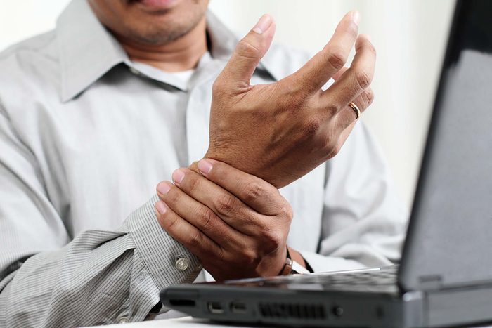 man holding his wrist in front of laptop