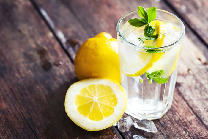 lemons on a wood table next to a glass of water with lemon slice and mint