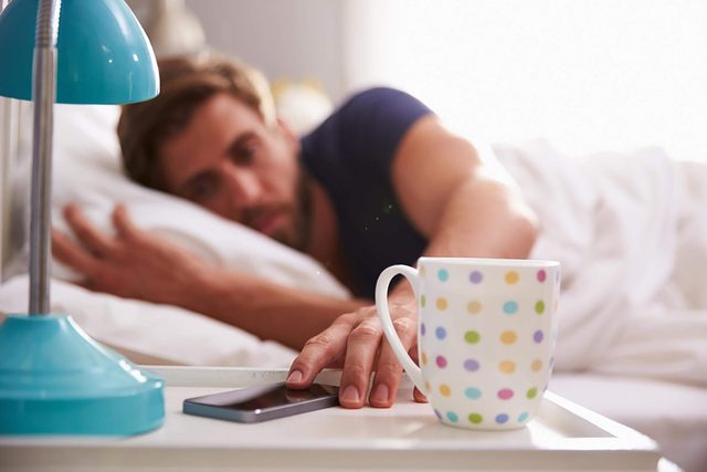 man in bed waking up and checking phone