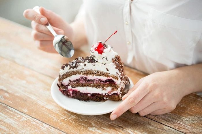 Person eating chocolate cream cake with cherry on top