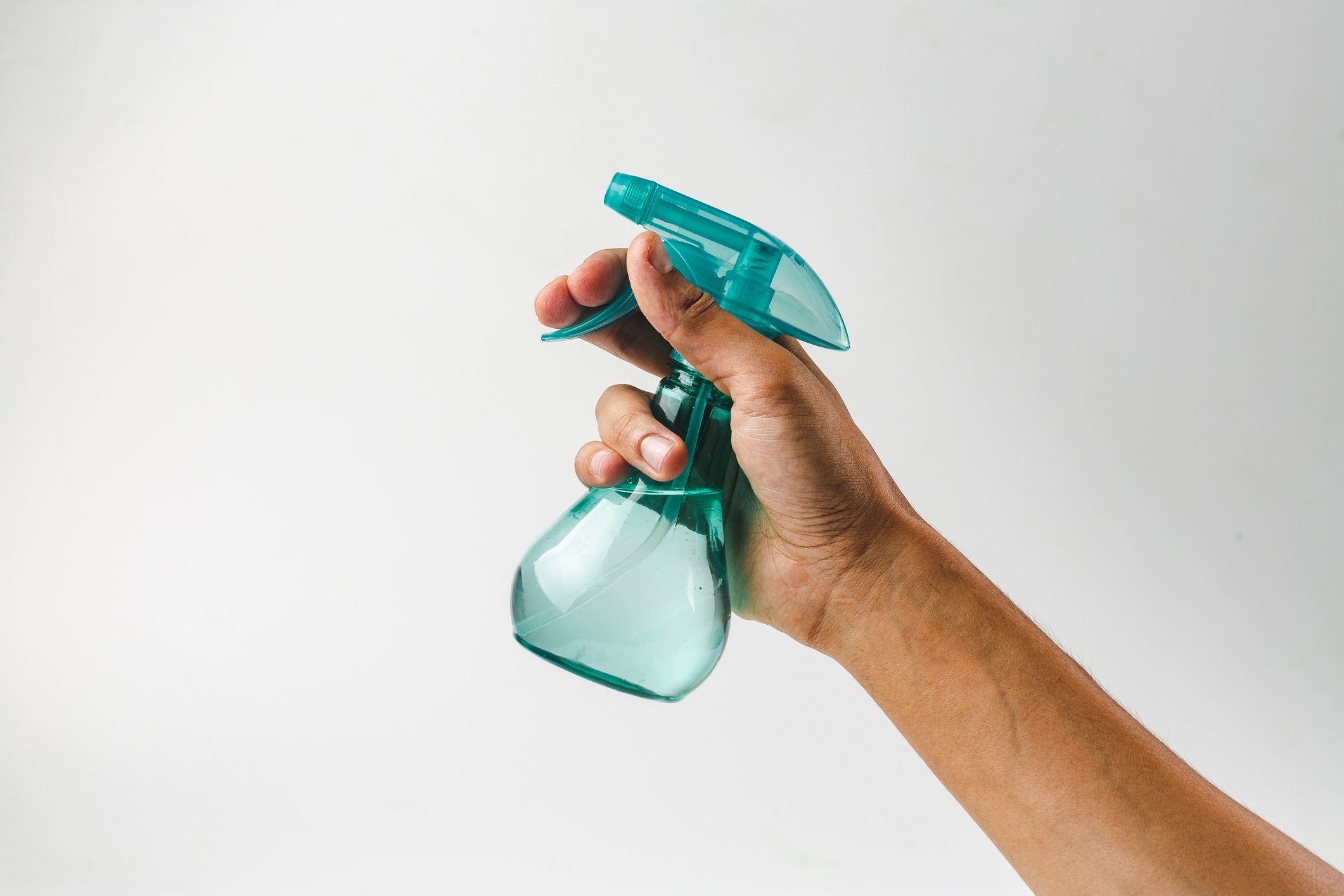 mão segurando um frasco de spray de plástico em fundo cinza