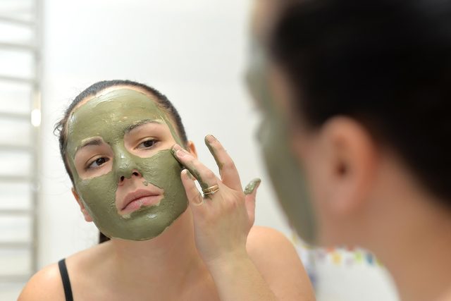 Young woman applying green Bentonite-Clay mask