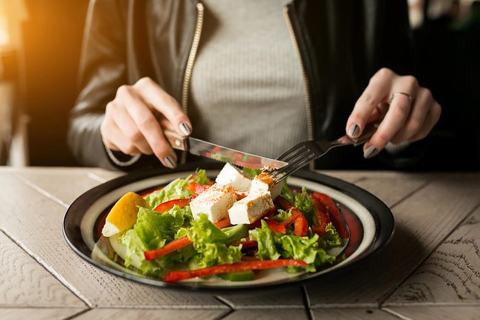 A woman eating a salad with a fork and knife at an outdoor table.
