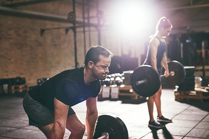 A man and woman doing barbell deadlifts in a gym.