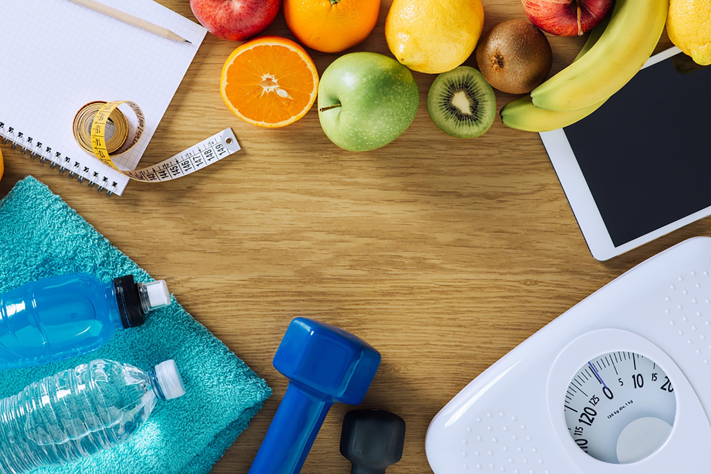 Items representing health including a scale, fruit, a free weight and a water bottle