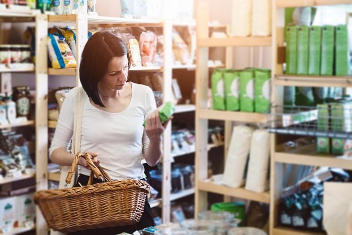 A woman carrying a basket is food shopping.