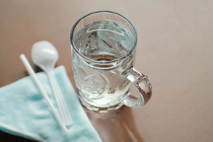 glass of water with blurred spoon, straw, and napkin on table