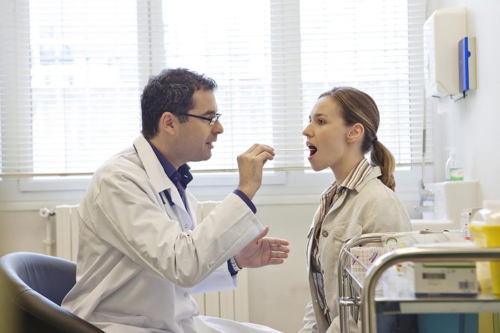 doctor placing a tongue depressor in a woman's mouth