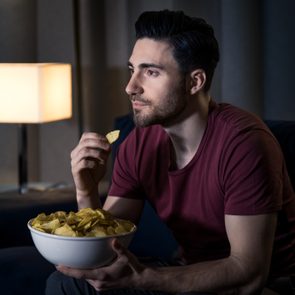man eating chips while watching a movie at home