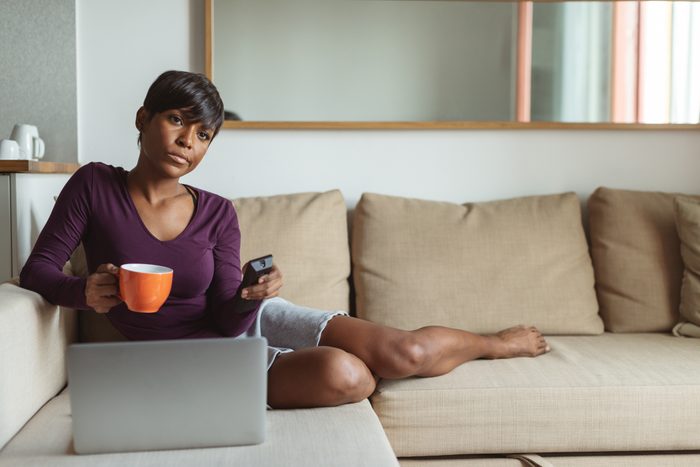 woman watching tv and using laptop on couch at home