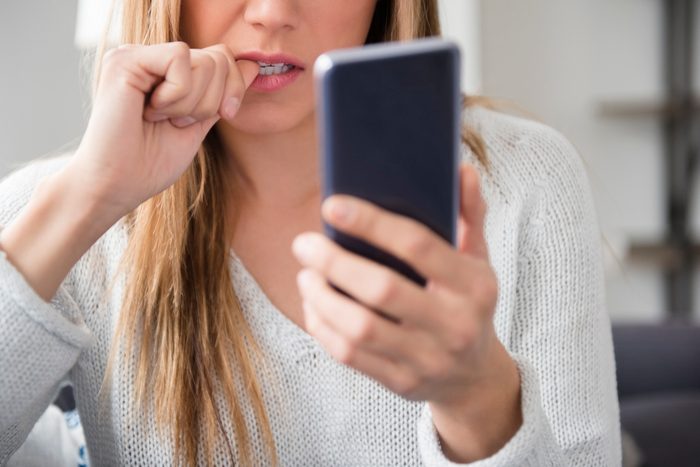 woman biting nails and looking at smartphone