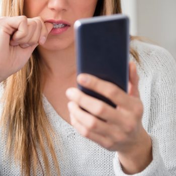 woman biting nails and looking at smartphone