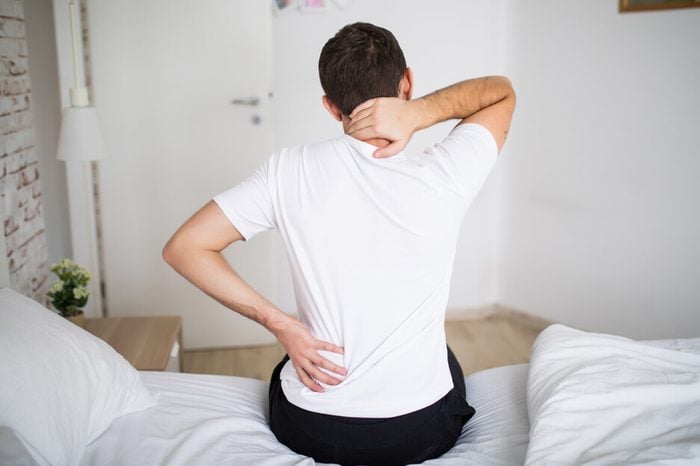 Man sitting on his bed, holding his back and having intercostal neuralgia.