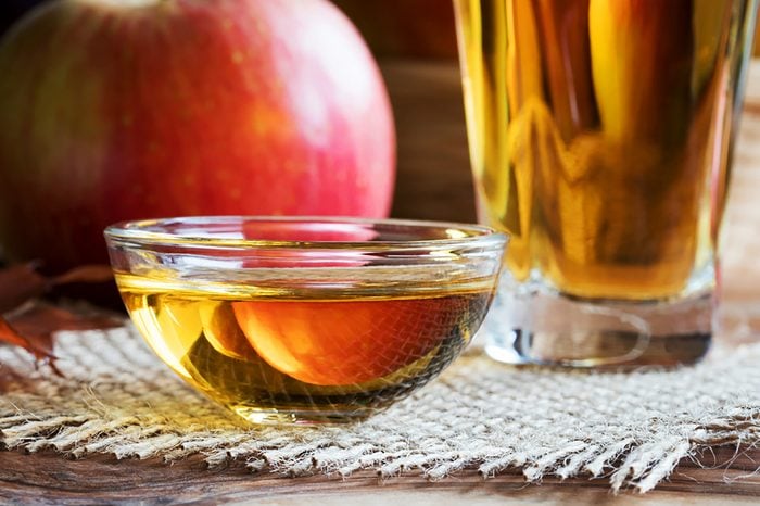 Apple-cider-vinegar in a bowl with glass of vinegar and an apple in the background