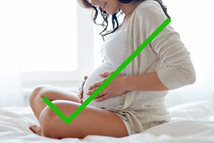 A pregnant woman on a bed with a check mark through it.