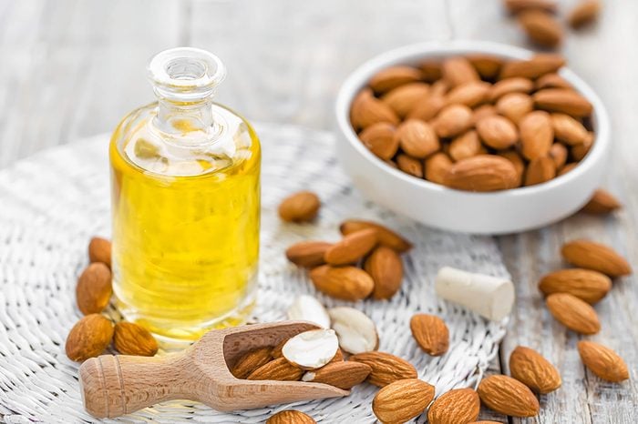 Almond-oil in a jar with bowl of almonds and scattered almonds