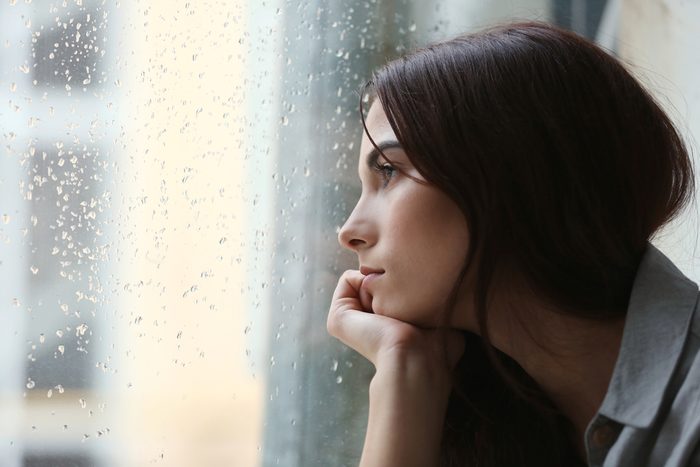 Depressed young woman looking out rainy window