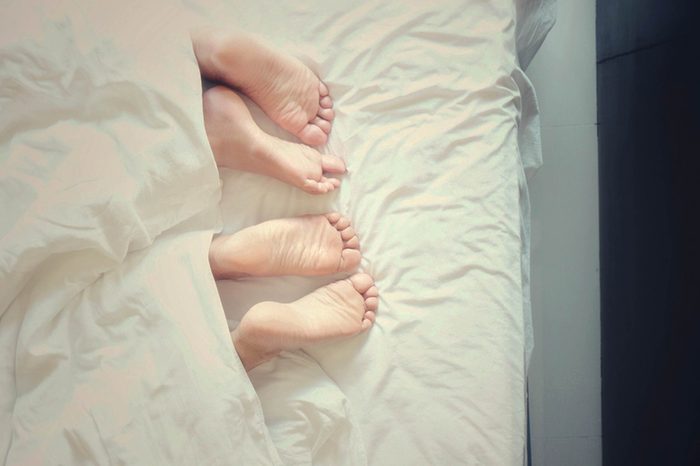 A couple's feet poking out of the bedcovers.