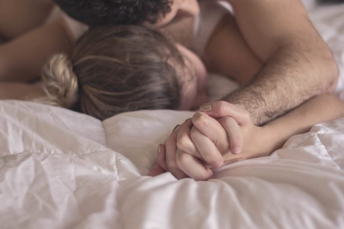 Man and woman in bed together holding hands.