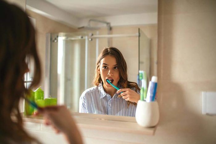 woman brushing teeth while looking in mirror