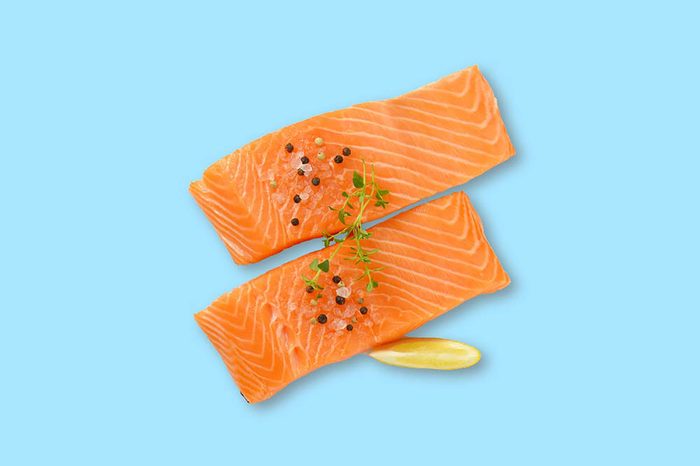 two fillets of salmon with pepper on top and a lemon wedge