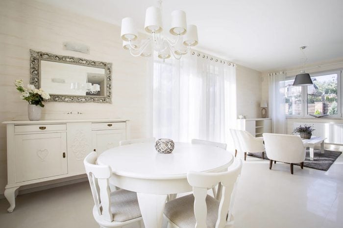 white dining table with white chairs in a white room with a mirror