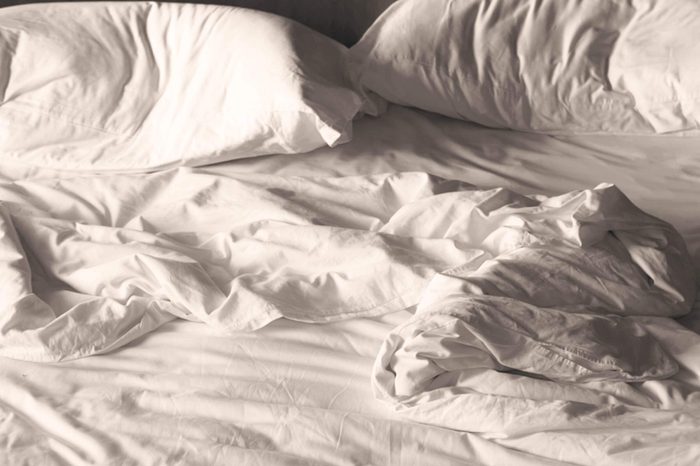 A messy, unmade bed with white sheets and pillows.