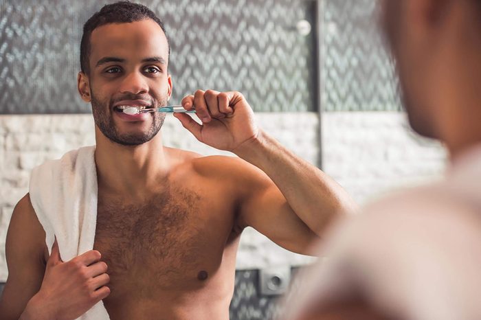 shirtless black man brushing teeth in mirror