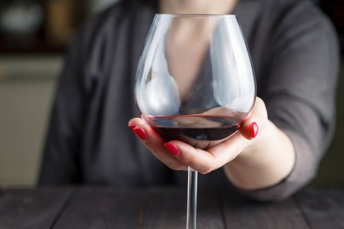 woman drinking alcohol on dark background. Focus on wine glass