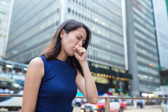 business woman in urban setting outdoors, coughing into her fist