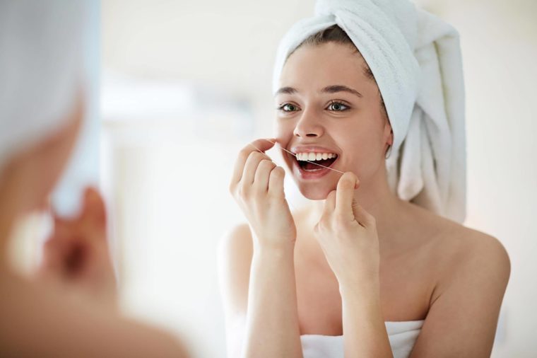 woman with towel around her hair flossing her teeth
