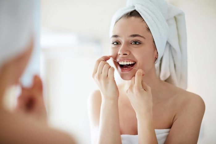 woman with towel around her hair flossing her teeth
