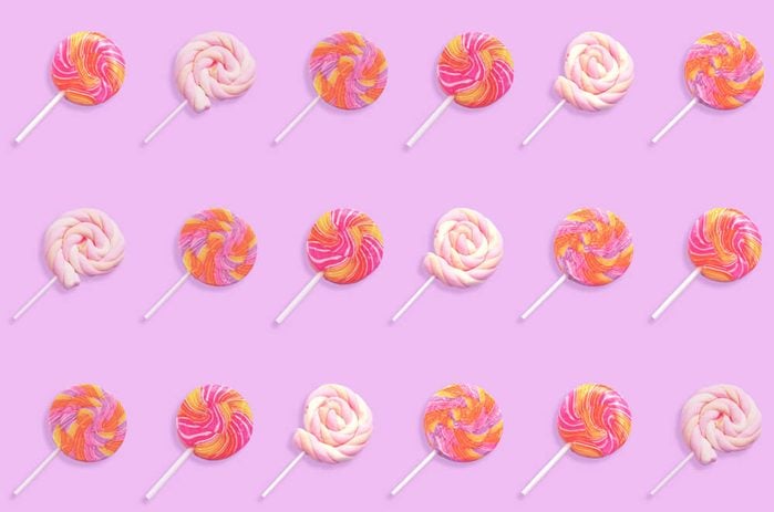 Pattern of colorful lollipop candy with stick isolated on violet background. Flat lay. 