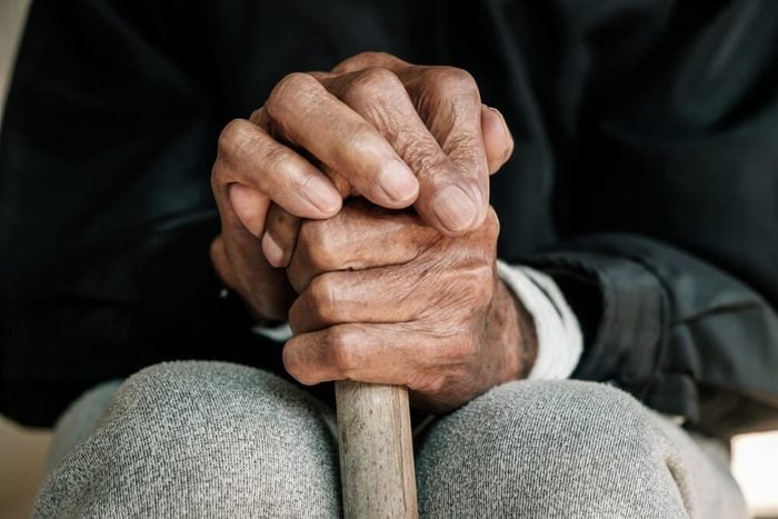 older man's hands holding on to a walking stick