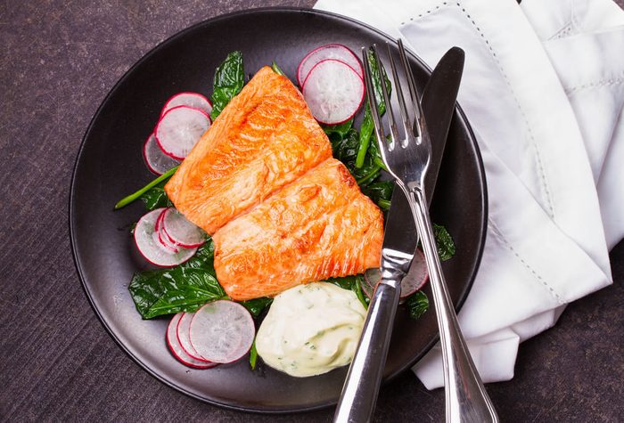 heart health diet; Broiled salmon with radish and spinach, served on black plate. View from above, top studio shot