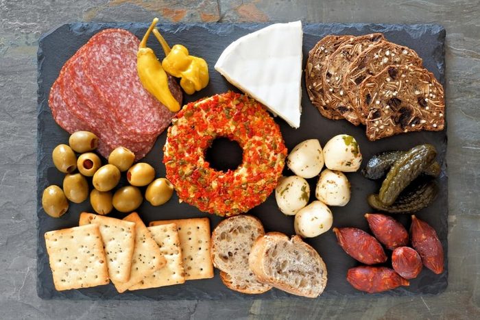 Appetizer platter with an assortment of cheeses, crackers, meats and snacks above view on a slate background