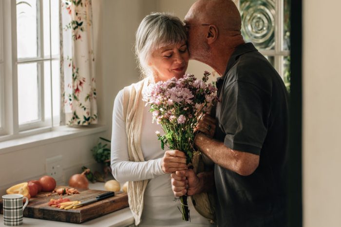 senior couple in kitchen husband giving wife flowers