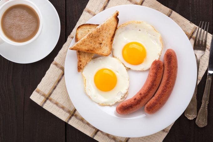 Delicious breakfast. Served on a wooden table with toast, eggs, sausage, wafers, coffee, orange juice, jam, knife, fork. Horizontal image. Top view. View from above